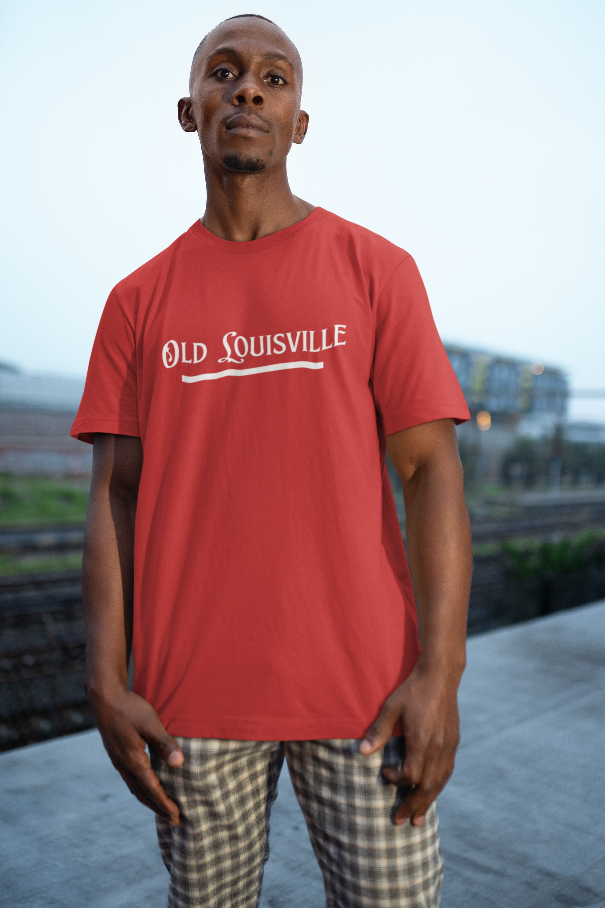 Man wearing a red 'Old Louisville' t-shirt standing outdoors with a blurred background